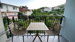Un balcón con dos sillas de metal y una mesa, con vista a una zona residencial con casas y vegetación.