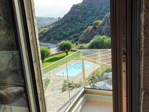 Vue depuis un balcon doté d’une balustrade en verre, donnant sur une piscine et un jardin aménagé.