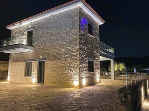 Un bâtiment en pierre doté d’un balcon, éclairé par des lampes extérieures.