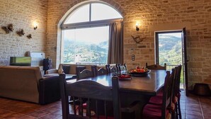 Un'area pranzo rustica con parete in pietra, un'ampia finestra ad arco e vista sulla campagna.