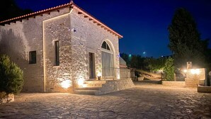 Un edificio in pietra con tetto in tegole, un'ampia finestra ad arco e un cortile pavimentato.