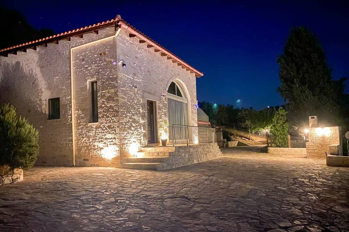 A stone building with a tiled roof, a large arched window, and a paved courtyard.