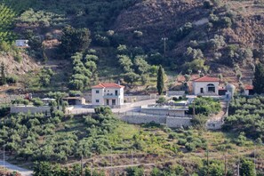 Il s’agit d’une propriété située sur une colline, comprenant plusieurs bâtiments, dont une maison principale avec un toit recouvert de tuiles rouges, ainsi qu’une dépendance plus petite à proximité.