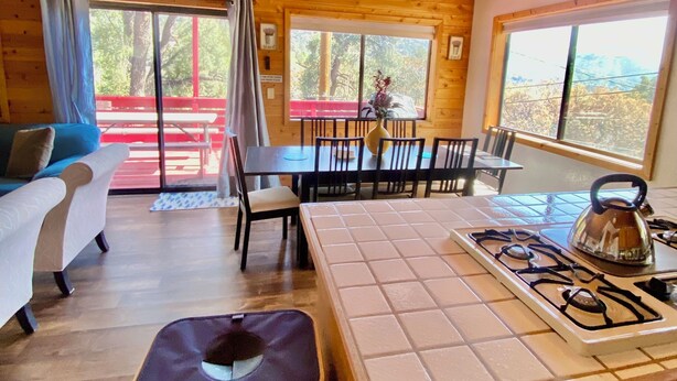 Een vakantiehuisje met een eettafel, stoelen, een keuken met een gasfornuis, een plafondventilator en een groot raam.