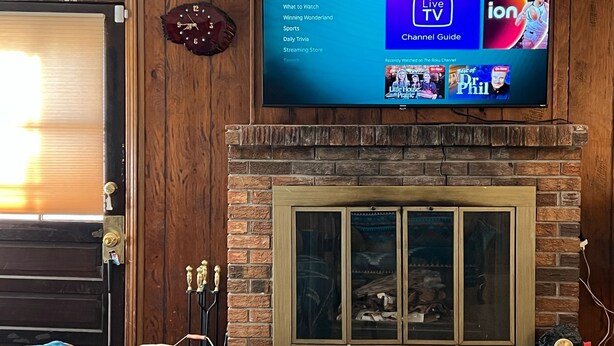 Una sala de estar con un televisor montado que muestra la interfaz de Roku, una chimenea con puerta de vidrio y una puerta de madera con manija de latón.