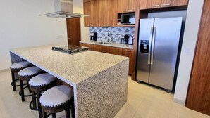 Una cocina con encimeras de granito, armarios de madera, un refrigerador de acero inoxidable y una estufa a gas integrada.