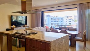 Una cocina moderna con una isla central, un área de comedor con sofá y sillas, y un ventanal con vistas a la ciudad.