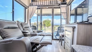 Un intérieur de camping-car moderne doté d’un espace repas modulable, d’une kitchenette et d’une grande porte-fenêtre coulissante offrant une vue panoramique.