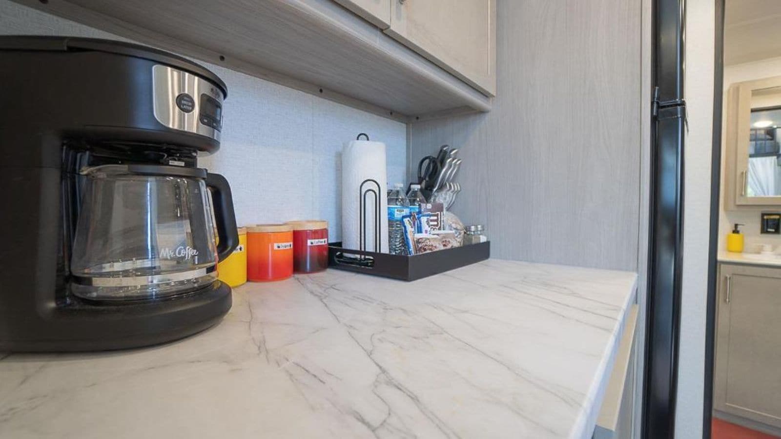 A kitchen with a coffee maker, storage containers, and utensils on the counter.