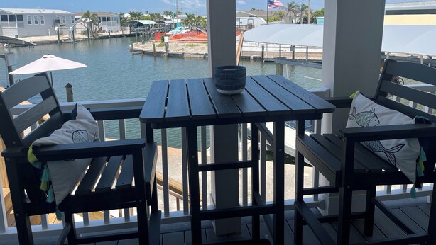 Una terraza de madera con una mesa y sillas, con vista a un puerto deportivo con barcos y un muelle.