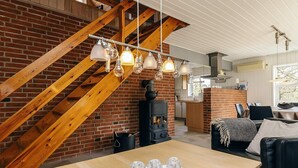 Ein gemütliches Interieur mit freiliegenden Holzbalken, einer Backsteinwand, einer modernen Küche und einem Essbereich mit Holztisch und Stühlen.