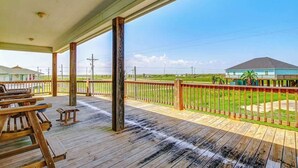 A wooden deck with picnic tables and a view of a golf course. - Best Little Shore House in Texas (Crystal Beach)
