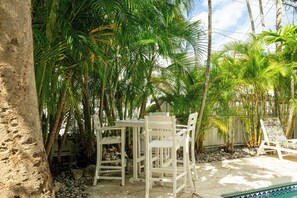 Un patio con mesa y sillas, rodeado de palmeras y una piscina.