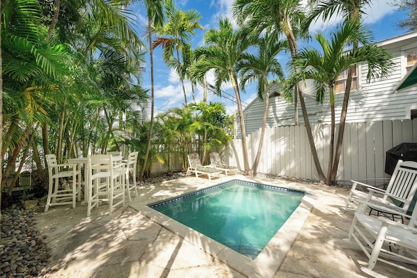 Patio con piscina rodeado de palmeras y una cerca blanca.