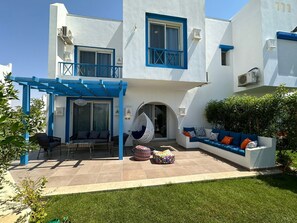 Un edificio de dos pisos con fachada blanca y detalles azules, que cuenta con un patio con asientos exteriores y una hamaca colgante.