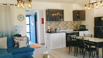 Une cuisine moderne avec des meubles blancs, un réfrigérateur noir et un coin repas avec des chaises noires.