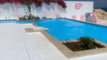 Une piscine dotée d’une terrasse blanche, entourée de fleurs rouges et d’un panneau indiquant « Club de plage réservé aux femmes ».
