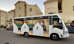 Un autobús blanco con un costado transparente estacionado frente a edificios residenciales.
