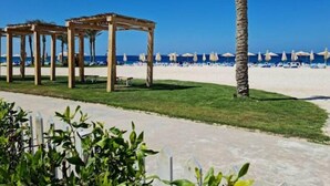 Una playa con pérgolas de madera, una palmera y sombrillas.