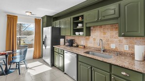 Une cuisine moderne avec des meubles de couleur verte, un plan de travail en granit, un évier en acier inoxydable et un four encastré.