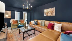 Un salon moderne avec un mur bleu foncé, un canapé en cuir marron, un fauteuil vert et un tapis à motifs.