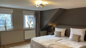 A bedroom with a large bed, a nightstand, a lamp, a window with curtains, and a view of buildings outside. - Vacation home Mosel-Wohnen I in Ferienland Cochem -balcony, sauna, garage (Bruttig-Fankel)
