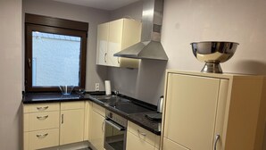 A compact kitchen with a built-in oven, a stainless steel range hood, and a window with a view. - Vacation home Mosel-Wohnen I in Ferienland Cochem -balcony, sauna, garage (Bruttig-Fankel)