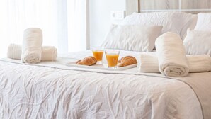 Un lit parfaitement fait, avec du linge de lit blanc, un plateau avec des croissants et du jus d’orange, et des serviettes enroulées.