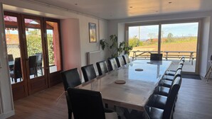Un comedor amplio con una mesa larga y sillas, ventanas grandes con vistas al exterior y una planta en maceta.