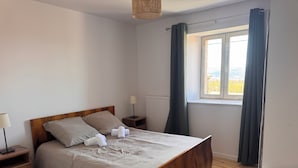 Una cama bien hecha con cabecera de madera, una mesita de noche con lámpara y una ventana con cortinas.