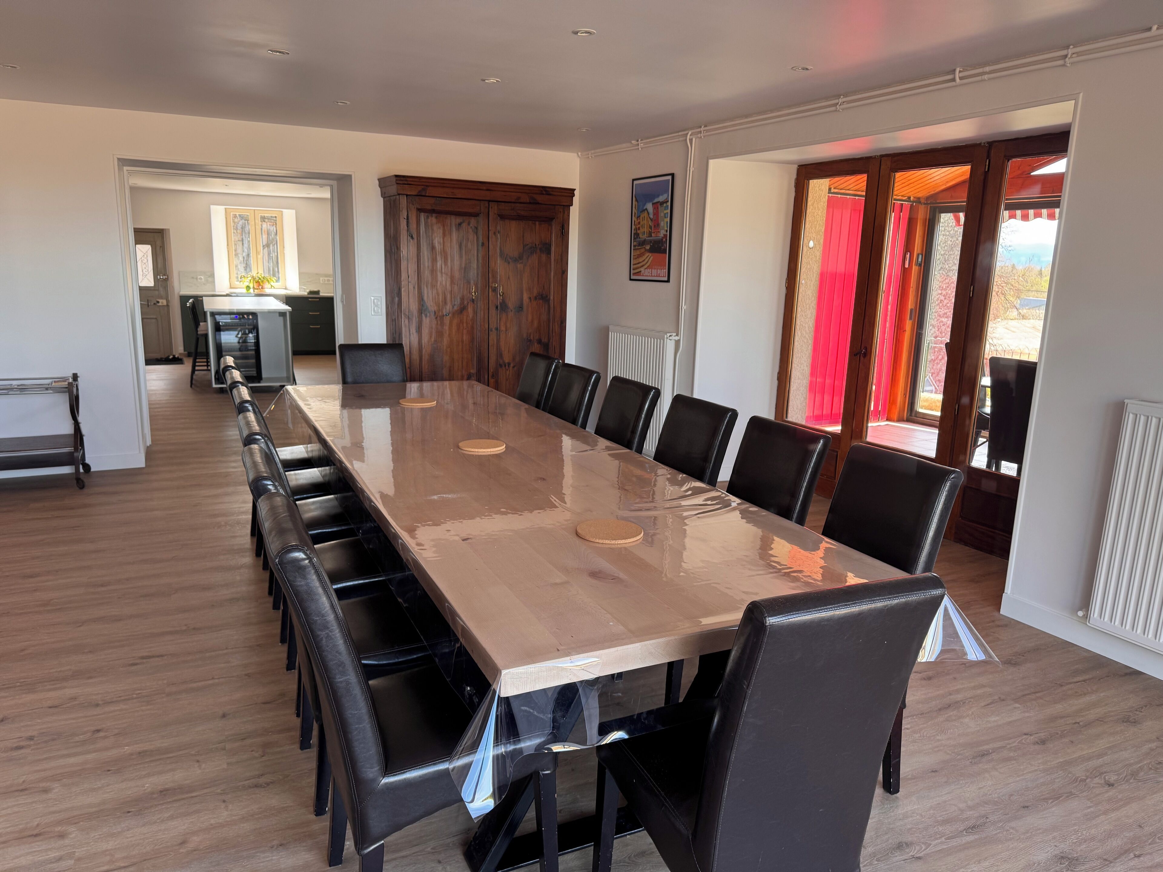 A conference room with a long table and chairs, a wooden cabinet, and a view through a glass door.