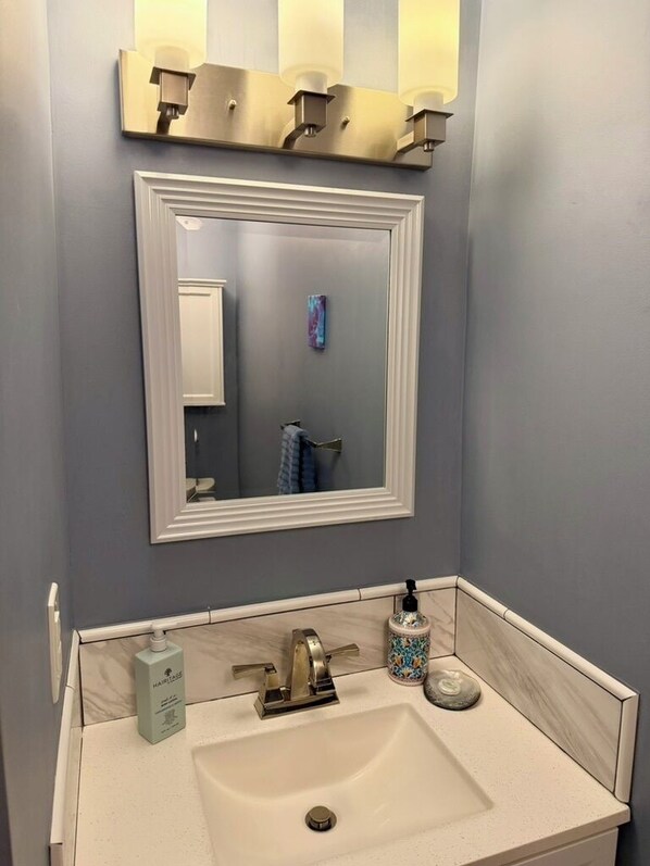 A bathroom with a white sink, a large mirror, and a wall-mounted light fixture.
