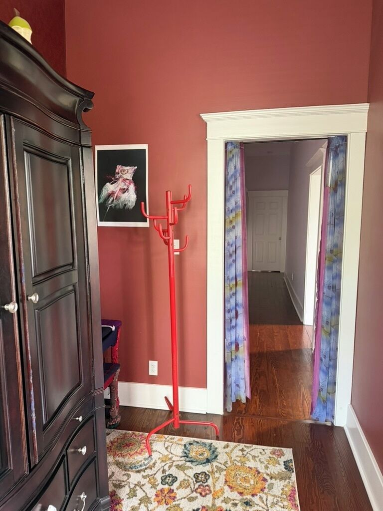 Een hal met een donker houten garderobe, een rode kapstok, een lijst met een afbeelding en een vloerkleed met dessin.
