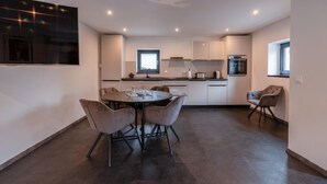 A modern kitchen with a dining area, featuring a round table with chairs, a built-in oven, and a window providing natural light.