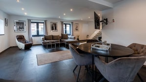 A modern living room with a sofa, armchair, and a dining table with chairs.