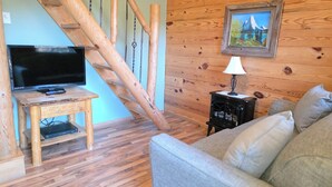 A cozy living room with a wooden staircase, a television on a wooden stand, a sofa, and a painting on the wall. - Timber Ridge #4 at Rustic Ridge (KEYSTONE)