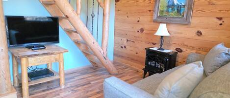 Una sala de estar acogedora con una escalera de madera, un televisor sobre un mueble de madera, un sofá y un cuadro en la pared.