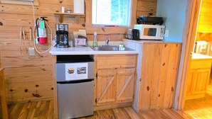 A compact kitchen with wooden cabinets, a stainless steel refrigerator, a coffee maker, a microwave, and a window above the sink. - Timber Ridge #4 at Rustic Ridge (KEYSTONE)