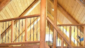 A wooden staircase with a TV on a wooden stand in a room with a high ceiling and wooden beams. - Timber Ridge #4 at Rustic Ridge (KEYSTONE)