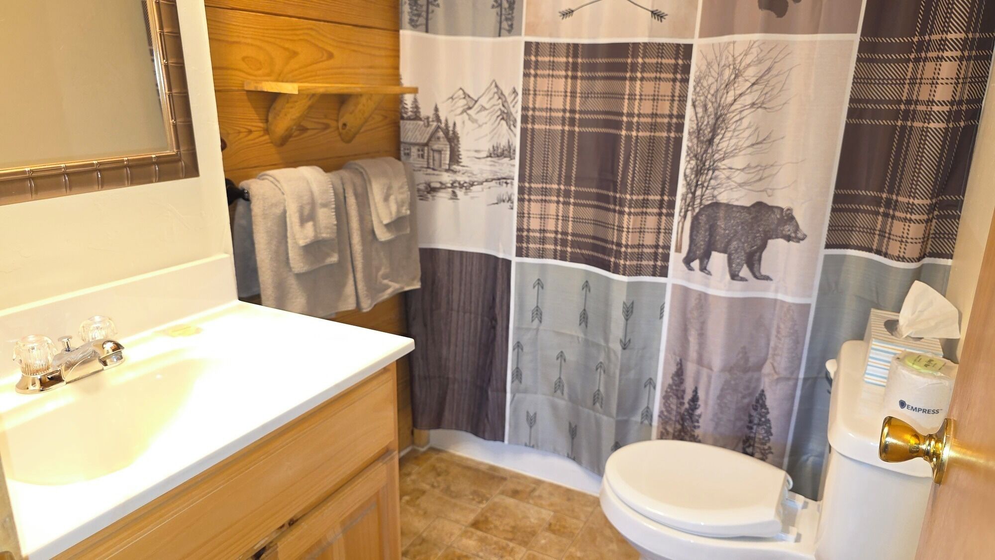 Un bagno con un mobile bagno in legno, un lavandino bianco, un water e una tenda da doccia a quadri.