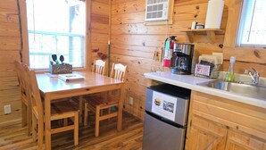 A wooden cabin interior with a dining table, chairs, a coffee maker, a refrigerator, and a sink. - Timber Ridge #4 at Rustic Ridge (KEYSTONE)