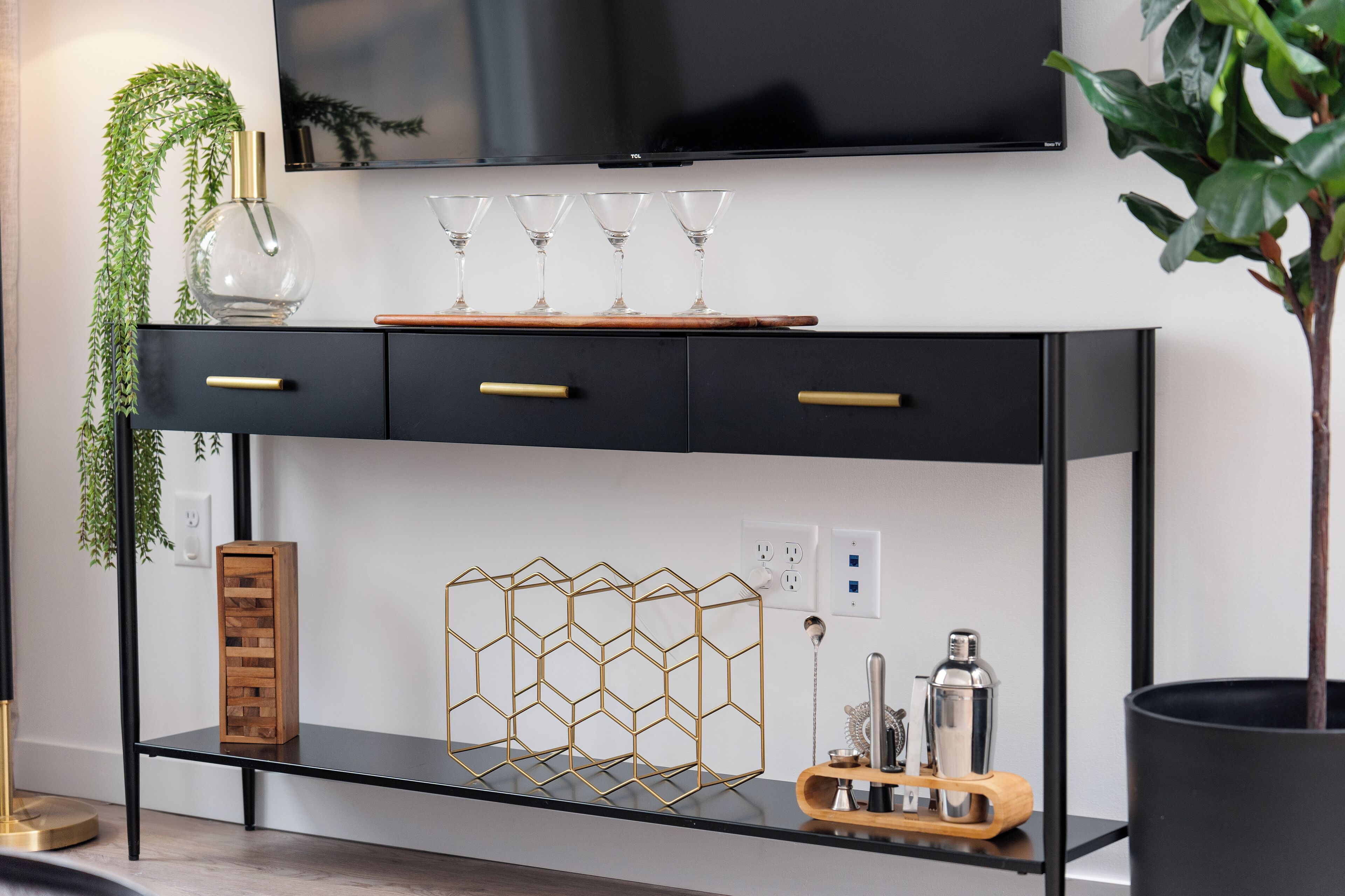 Una sala moderna con un mueble bajo para televisor negro, una mesita de madera y un florero de vidrio con una planta.