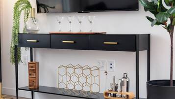 Una sala moderna con un mueble bajo para televisor negro, una mesita de madera y un florero de vidrio con una planta.