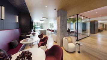 A modern office space with a mix of seating areas, including a red sofa and round tables, a glass partition, and a wooden floor.