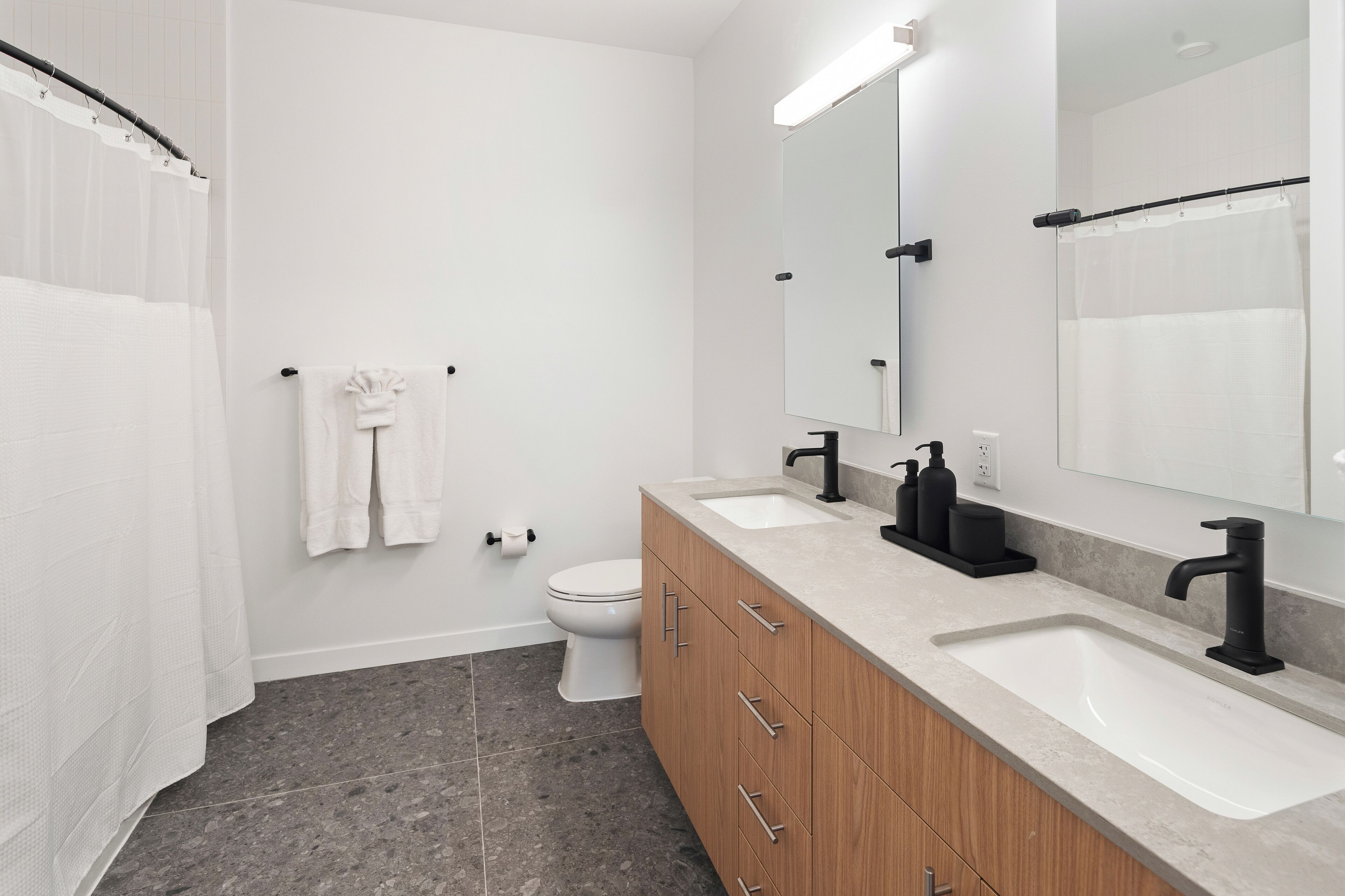A modern bathroom with a double sink, wooden vanity, and a large mirror.