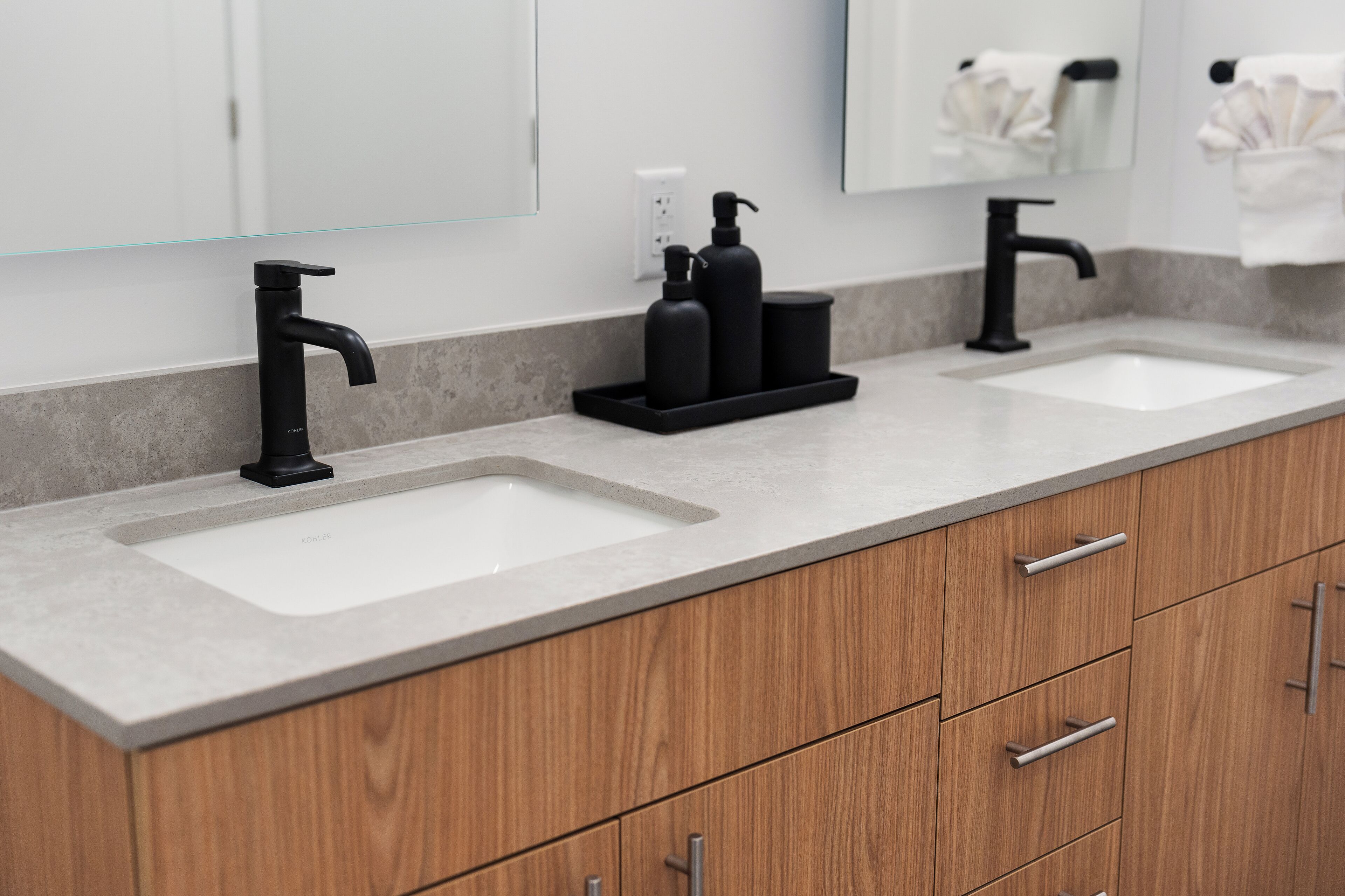A modern bathroom with two sinks, a black faucet, and a wooden cabinet with drawers.