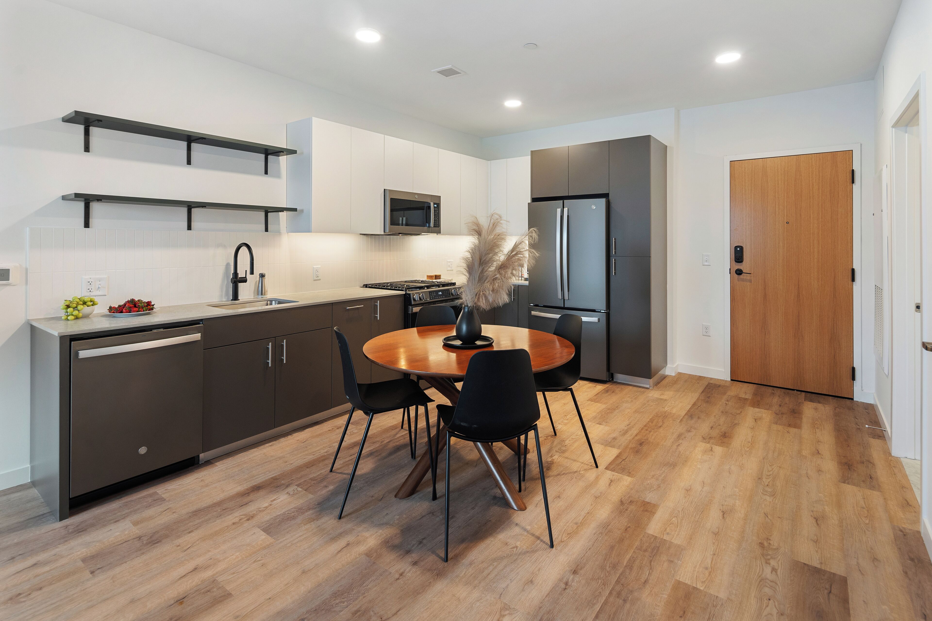 A modern kitchen with dark cabinets, a wooden dining table, and black chairs.