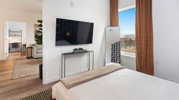 A hotel room with a bed, a TV mounted on the wall, a small table with a plant, and a window with curtains.