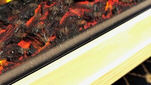 A close-up of a grill with visible flames and charred food. - The Cottage (Mikana)