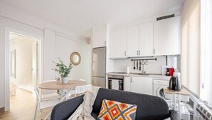 A modern kitchen with white cabinets, a dining area with a round table, and a living room with a sofa and decorative pillows. - Apartment in Sotrondio near the Nalon river (San Martin del Rey Aurelio)